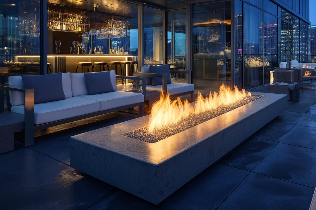 Modern rooftop lounge featuring a sleek commercial fire pit with vibrant flames, surrounded by contemporary seating and city skyline views at dusk.