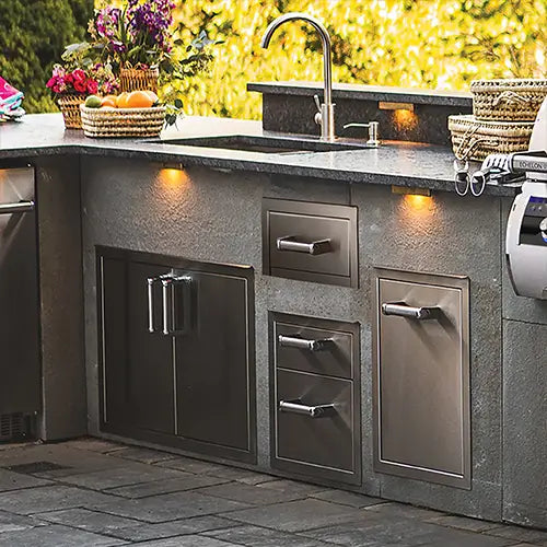 An outdoor kitchen showcases it's stainless steel drawers and doors below an outdoor sink