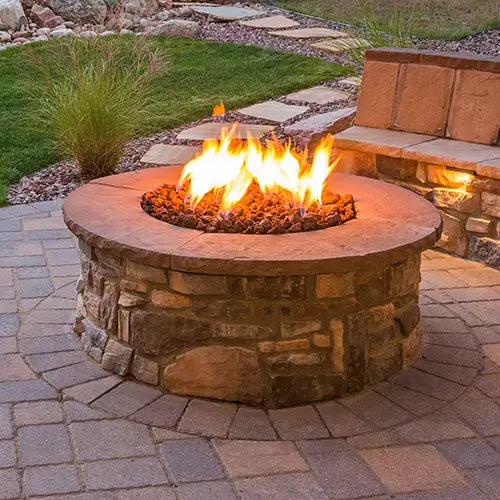 A stone walled DIY outdoor fire pit is ignited and ready to receive guests in the backyard at dusk