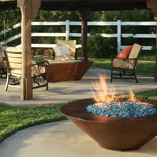2 copper fire pits are ignited on a relaxing patio in between a patio set and underneath a pergola