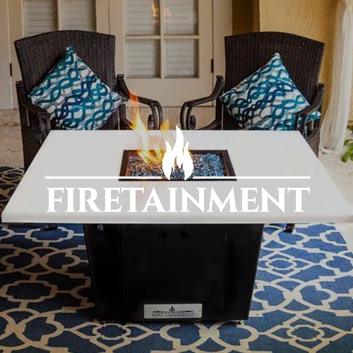Firetainment fire pit table with a sleek modern design, featuring a durable white tabletop and vibrant flames over glass media. Positioned in an elegant patio setup with patterned cushions and a stylish rug.