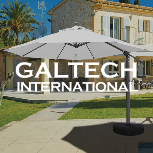 Galtech International patio umbrella with a sturdy base, offering ample shade over a sunlit outdoor space featuring a stone walkway, lush green grass, and a Mediterranean-style house with rustic charm.