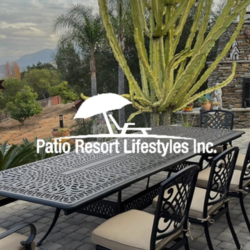Patio Resort Lifestyles Inc. ornate outdoor dining set featuring an elongated cast aluminum table with matching cushioned chairs, set on a stone patio surrounded by lush landscaping and mountain views.
