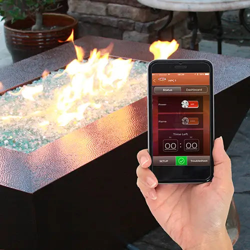 A smart phone is displaying the control app for the electronic ignition system for the copper fire pit in a backyard