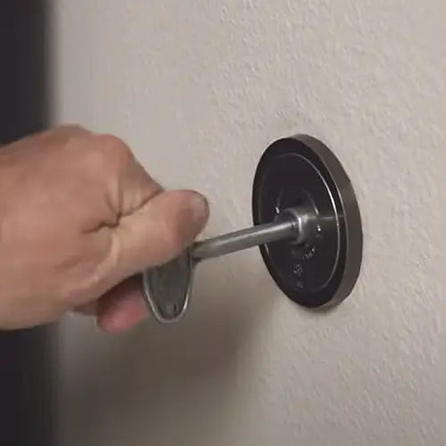 A closeup of a steel key valve is being turned to the on position by someones hand