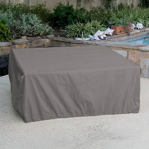 A gray fire pit cover is displayed in a simple backyard