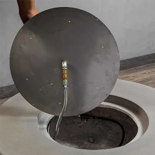 a fire pit burner pan is being lifted out of a fire pit to be show to the viewer