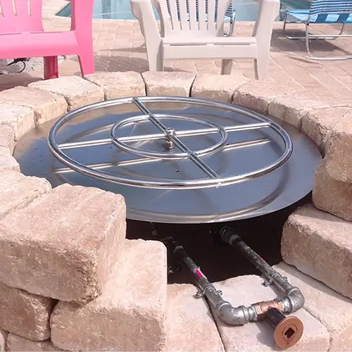 An exposed collection of gas fire pit parts is showing the inside parts for an outdoor fire pit by the pool