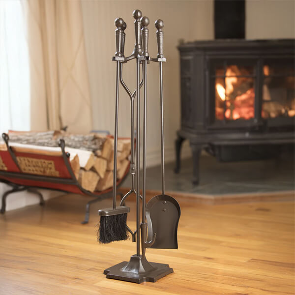 A fireplace tool set is on display near a wood pile and wood burning fireplace in a living room.