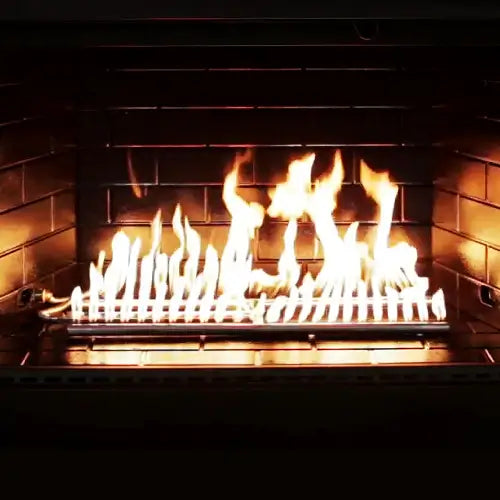 A stainless steel h-burner is lit inside a dark stone fireplace