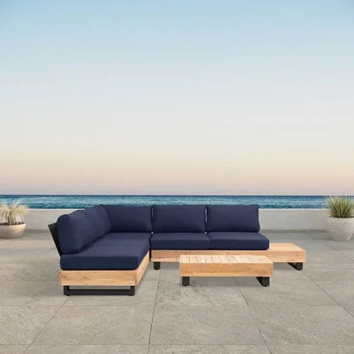 A stunning outdoor sectional sofa set with a wooden base, deep navy blue cushions, and a matching low-profile coffee table, overlooking an oceanfront setting.