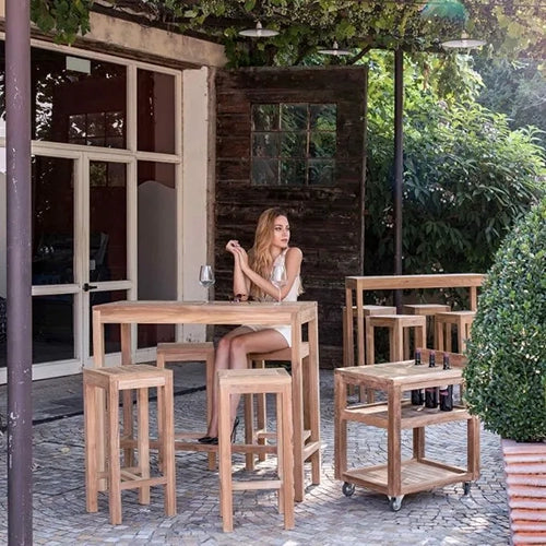 The Harmonia Living Vino Bar Set features a high-top teak table with matching barstools, offering a stylish and functional outdoor entertainment setup. 