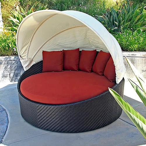 The Harmonia Living Wink Round Outdoor Daybed features a luxurious circular wicker base with plush red cushions and a retractable canopy for shade. Ideal for poolside relaxation, outdoor lounge seating, modern patio furniture, all-weather wicker daybeds.