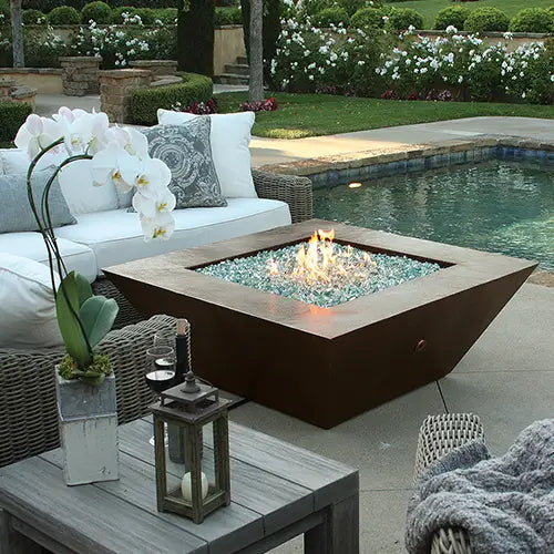 a hand-hammered copper moreno fire pit sits between an outdoor furniture set with candle lantern and hibiscus flower and an outdoor pool in the backyard