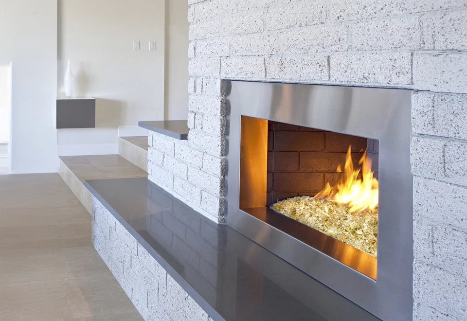 Modern gas fireplace with a sleek stainless steel frame, featuring 1/4-inch broken fire glass and a vibrant yellow flame against white brick.