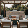 Beneath a wood pergola beside a built-in outdoor kitchen and stainless grill, a graphite concrete fire pit burns steadily in the center of a tiled seating area, its square opening filled with dark stones and golden flames while cushioned wooden chairs and sofas with soft pastel pillows form a circle around it, creating a patio fire pit that doubles as a modern square fire pit for relaxed outdoor entertaining framed by tall greenery in the background.