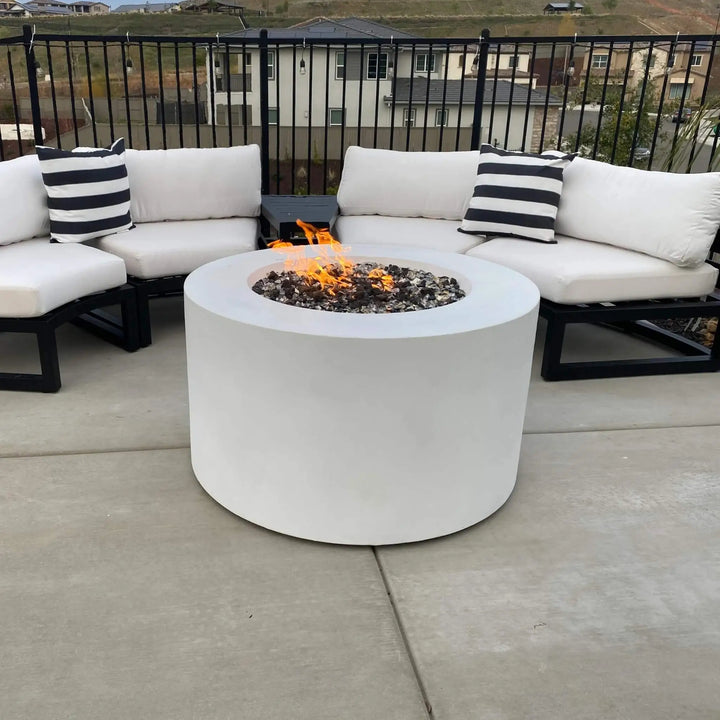 Modern outdoor patio setup featuring a 42-inch round white concrete fire pit with hidden propane tank by Starfire Designs, surrounded by cushioned sectional seating and black metal frames / perfect for cozy evenings and backyard gatherings.