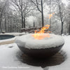 Customer photo of a round copper fire pit covered with snow, with flames flickering amidst the snow, set on a wooden deck overlooking a snow-covered landscape and trees