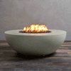 A studio close-up presents a round fire pit in a smooth natural gray finish, resting on a dark wood floor. Bright yellow flames burn centrally from a bed of black lava rocks, highlighting the curved profile of the concrete fire pit. This minimalist view emphasizes the sculptural design and consistent flame height typical of a high-quality natural gas fire pit or fire bowl installation.