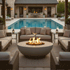 A spacious U-shaped seating area surrounds a grey round fire pit under a poolside pergola. The fire bowl serves as the centerpiece of this outdoor entertaining space, with flames providing warmth and ambiance. The setting features a large swimming pool and stone architecture, creating a luxurious backyard oasis. This setup is ideal for a family gathering fire pit experience, utilizing a clean-burning propane fire pit.