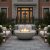A formal courtyard setting features a grey luxury fire pit positioned centrally on a bluestone patio with brick accents. Elegant sofas and lanterns surround the round fire pit, framed by a classic brick residence. The warm amber flames of the gas fire pit illuminate the seating area, serving as a sophisticated patio fire pit anchor for evening relaxation.