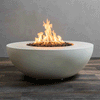 A wide shallow fire bowl made of smooth pale gray concrete rests on a striped wood-look floor in front of a plain wall, its circular opening filled with rough dark lava rocks while tall yellow flames from the gas fire pit rise and curl in the center, clearly showing the low rounded profile, slightly recessed rim, and small feet lifting this concrete fire pit a few inches above the ground.