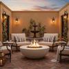 In a brick-paved courtyard framed by stucco walls, climbing vines, and a tiered fountain, cushioned metal lounge chairs with striped pillows encircle a low round fire bowl whose bright flames flicker above dark stones, lanterns and drinks resting on nearby tables, creating a sheltered patio fire pit scene where the outdoor fire pit naturally anchors conversation and relaxed outdoor entertaining at dusk.
