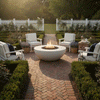 A white fire bowl sits at the center of a brick herringbone path in a manicured garden, its round fire pit opening filled with dark stones and a steady golden flame, while white Adirondack-style chairs, clipped boxwood hedges, lavender planters, and a white picket fence frame the view, so the backyard fire pit appears as the warm heart of a small backyard oasis designed for quiet conversation at sunset.