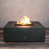A deep graphite concrete fire pit with crisp square sides sits centered on a striped wood-look floor against a soft taupe wall, its recessed square opening filled with chunky brown lava rocks while bright yellow flames from the gas fire pit rise and sway in the middle, clearly revealing the broad top surface, small metal control on the front, and low profile of this compact square fire pit as it flickers steadily in place.