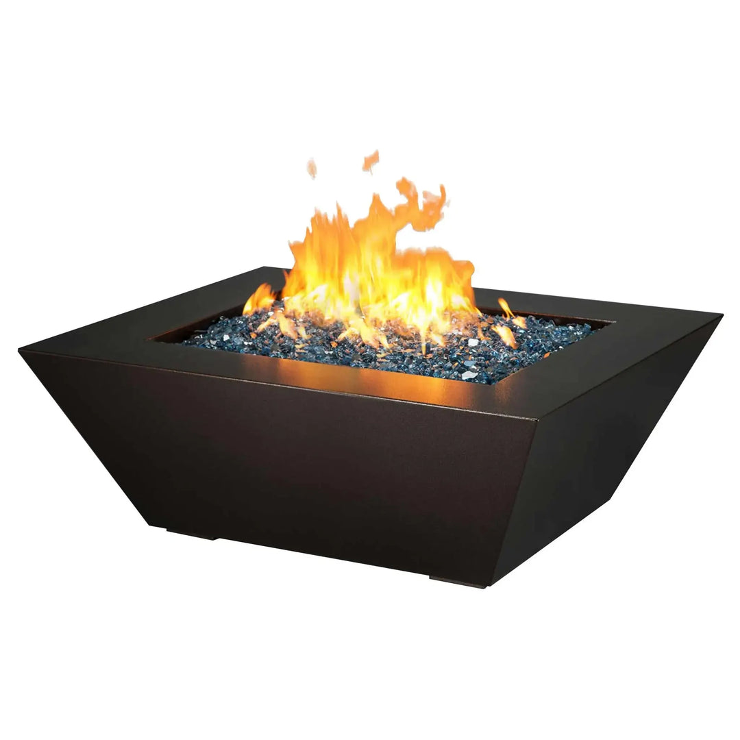 Trapezoidal fire pit with a modern design, filled with blue fire glass and vibrant flames, set against a plain white background.