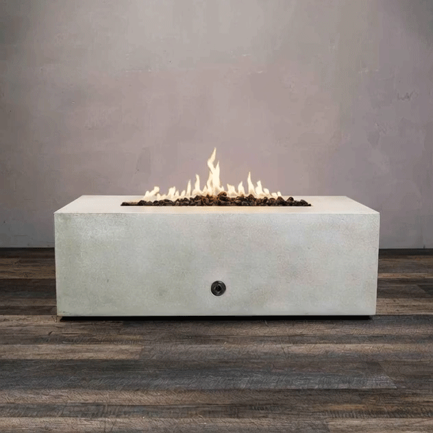 A low white concrete fire pit with a clean rectangular form sits on a wood plank floor against a smooth gray wall, flames rising in a long central channel over dark stones, and the GIF cycles as the steady glow from this concrete fire pit emphasizes its sharp edges, muted color, and low modern profile, presenting a streamlined modern fire pit that appears to run on an even-burning gas fire pit burner in a linear fire pit layout.