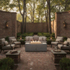 Inside a brick-walled courtyard with neatly trimmed hedges and tall trees, a pale gray concrete fire pit burns in a straight line of flames atop a herringbone brick patio, surrounded by cushioned armchairs and lanterns on low brick pillars, the patio fire pit acting as a central linear fire feature where the steady glow draws the seating group into an intimate family gathering fire pit arrangement.