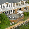 Aerial view of a stunning waterfront patio featuring a modern graphite-colored 55-inch rectangular Beton Concrete GFRC gas fire pit by Starfire Designs, surrounded by cozy white cushioned seating and a large cantilever umbrella, creating an inviting outdoor living space at a brick and white coastal home.