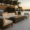 A waterfront terrace features a graphite outdoor fire pit positioned between a sofa and armchairs. The setting overlooks a bay with palm trees, creating a relaxing backyard oasis. The steady flames of the fire feature provide warmth and ambiance, with the gas fire pit serving as a focal point for evening gatherings.