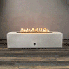 Alt Text: A studio presentation features a rectangular fire pit in a crisp white finish, resting on a dark wood floor. Bright yellow flames burn steadily along the linear fire pit