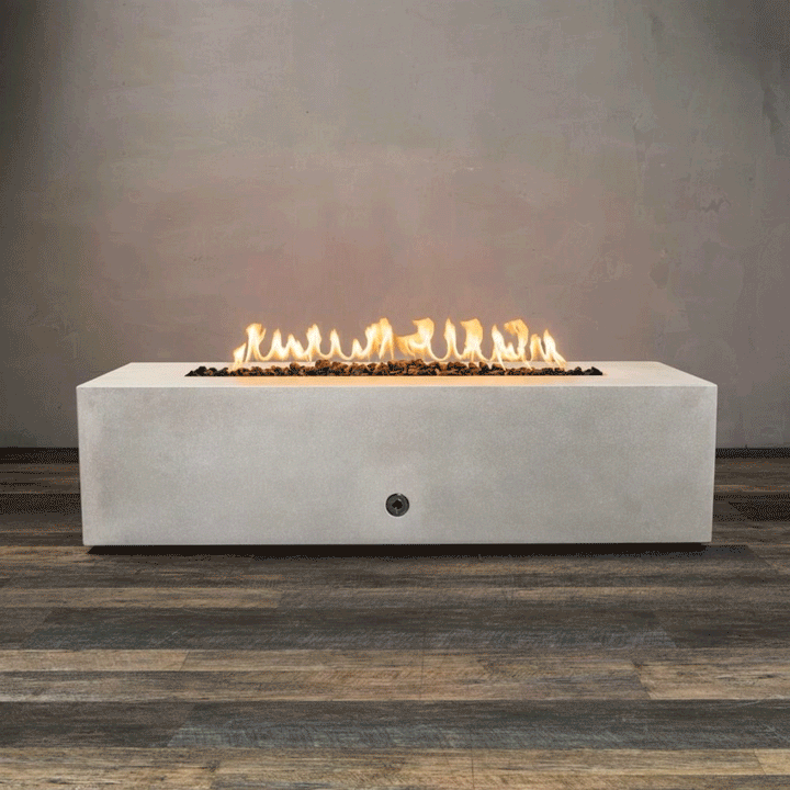 Alt Text: A studio presentation features a rectangular fire pit in a crisp white finish, resting on a dark wood floor. Bright yellow flames burn steadily along the linear fire pit