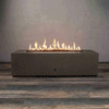 A low rectangular concrete fire pit designed as a sleek gas fire pit burns in a steady line of golden flames above small lava rocks, the sturdy fire table resting on a wide plank floor against a simple gray wall, while the GIF loops through the gentle flicker of the fire, emphasizing the long, narrow opening, crisp corners, warm reflections on the floor, and solid brown body of this rectangular fire pit in a quiet, uncluttered studio setting.