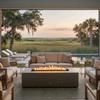 A soft beige sofa and matching armchairs are arranged in a U-shape around a low concrete fire pit on a covered terrace, the slim rectangular burner producing a bright, continuous line of flame as it reflects off nearby pool water and the marshy coastal landscape beyond, creating a sheltered patio fire pit nook that reads as a cozy backyard fire pit and versatile outdoor fire pit lounge for quiet sunset views and conversation.