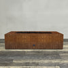 A side view of the 60" x 32" Rectangle Gravity Corten Steel Fire Pit by Starfire Designs - perfect for outdoor patio spaces. Natural gas or propane compatible, enhancing warmth and ambiance. Lava rocks included for added aesthetic.