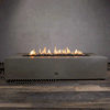 A studio presentation displays a large rectangular fire pit in a natural brown finish, resting on a dark wood floor. Bright yellow flames burn continuously along the linear fire pit burner, rising from a bed of black lava rocks. The visible chrome key valve on the side indicates the manual control of this concrete fire pit, highlighting the earth-tone texture and clean operation of a natural gas fire pit connection.