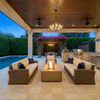 A covered poolside cabana features a brown patio fire pit surrounded by wicker sofas and armchairs. The setting overlooks a swimming pool and bougainvillea-covered pergola, creating a luxurious backyard oasis. The clean-burning flames of the smokeless fire pit provide ambiance for the outdoor living room, utilizing a propane fire pit setup for convenience.
