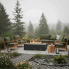On a misty garden terrace bordered by wild grasses and flowers, a dark graphite concrete fire pit burns with a bright linear flame between green-cushioned wooden chairs and a matching sofa, lanterns resting on the paver edges and tall fir trees fading into the fog beyond, creating an outdoor fire pit that feels like a cozy backyard fire pit and relaxed family gathering fire pit nestled quietly in a soft forest landscape at dusk.