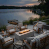 On a stepped stone patio beside a calm lake at dusk, a white rectangular concrete fire pit glows between matching wood-framed lounge chairs and a sofa, its continuous row of flames reflecting softly on the water while lanterns, grasses, and a small dock with kayaks frame the scene, showing an outdoor fire pit used as a cozy backyard fire pit and inviting family gathering fire pit as the sky darkens.