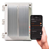 Bromic 2-Channel Smart-Heat Dimmer shown with its aluminum cooling fins and a smartphone displaying the Bromic app, demonstrating wireless heater control and adjustable heat settings.