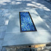 Rectangular oil-rubbed bronze fire pit burner filled with a custom pre-mix of sparkling blue fire glass, adding modern elegance to a stone patio design.