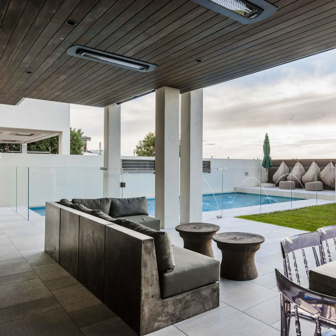 Modern covered patio with recessed Bromic Heating Tungsten Smart-Heat Electric Heaters in black, providing cozy warmth above a contemporary outdoor lounge and poolside seating area.
