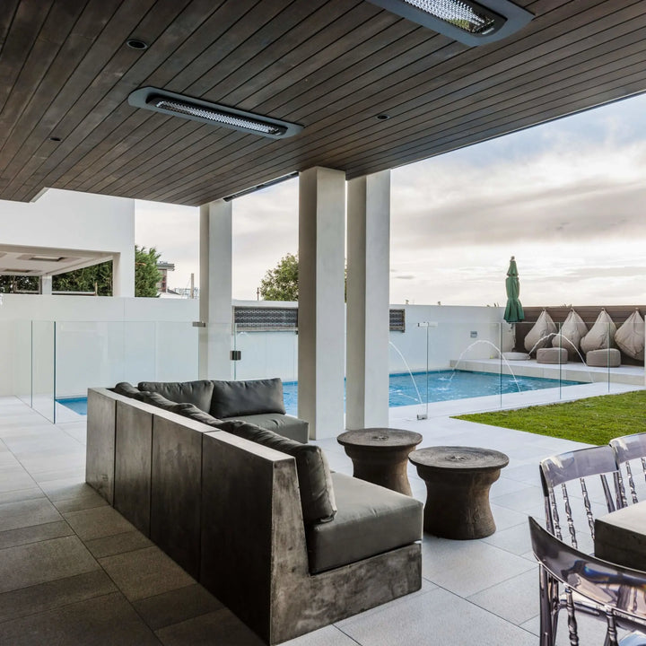 Modern covered patio with recessed Bromic Heating Tungsten Smart-Heat Electric Heaters in black, providing cozy warmth above a contemporary outdoor lounge and poolside seating area.