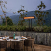 Elegant outdoor restaurant terrace with Bromic Tungsten Electric Smart-Heat heater on a post mount, providing gentle warmth over a dining table surrounded by mountain views.