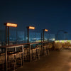 Nighttime rooftop bar with several Bromic Tungsten Electric Smart-Heat heaters, creating a comfortable outdoor experience with warm amber lighting and scenic skyline views.