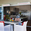 Elegant outdoor dining space blending indoor and outdoor living, featuring white Bromic Tungsten Electric Smart-Heat heaters above a wicker table set with bright red and white décor.